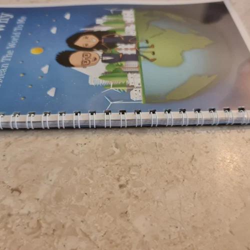 Coil bound photo book lying flat on a marble surface, showing sturdy white spiral binding and laminated cover design.